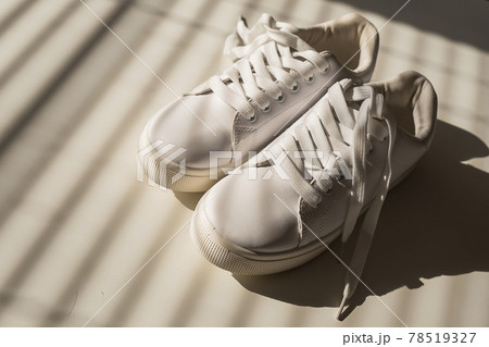 Close-up of women's white leather sneakers in the shade of the blinds. 78519327