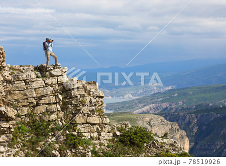 Young woman with backpack standing on cliff's edge and taking a photo 78519926