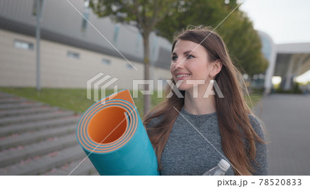 Portrait of a beautiful fitness girl. The Young Girl Goes Slowly To The Camera And Smiles. Active people. Inspiration and motivation. Active woman with fitness mat and water bottle in hands walking 78520833