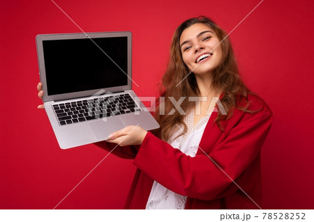 Photo of beautiful young woman holding computer laptop looking at camera isolated over colourful 78528252
