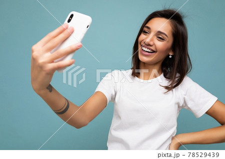 Attractive charming young smiling happy woman holding and using mobile phone taking selfie wearing 78529439