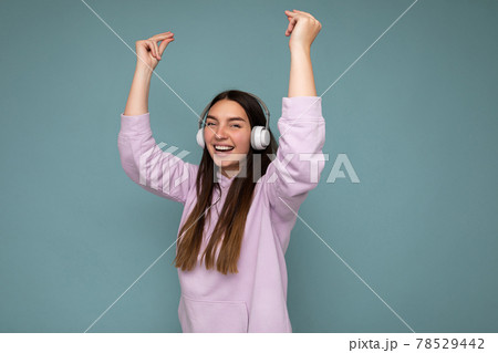 Attractive positive smiling young brunette woman wearing light purple hoodie isolated over blue Attractive positive smiling young brunette woman wearing light purple hoodie isolated over blue 78529442