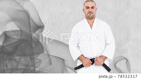 Composition of caucasian male martial artist with black belt over trails of smoke o grey background 78532317