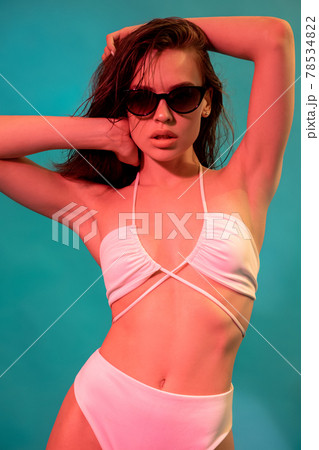 Young woman in white swimsuit and sunglasses on blue background 78534822
