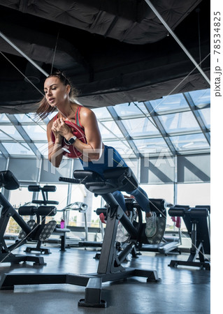 Young woman doing hyperextension with weight plate at gym 78534825