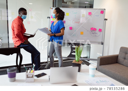 Diverse male and female colleague in face masks discussing paperwork in office Diverse male and female colleague in face masks discussing paperwork in office 78535286