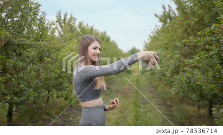 Young Attractive Sports Girl Shooting on a Phone Tree Photographed Against Nature Background. Girl blogger points to the camera nature, the concept of stories about the environment protection of trees Young Attractive Sports Girl Shooting on a Phone Tree Photographed Against Nature Background. Girl blogger points to the camera nature, the concept of stories about the environment protection of trees 78536714