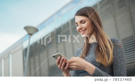 Close-up Of A Young Beautiful Sports Fitness Girl Holding A Smartphone In The Hands, Using A Fitness App. Modern City Shooting On the Street. Portrait woman looking at smartphone while running outdoor Close-up Of A Young Beautiful Sports Fitness Girl Holding A Smartphone In The Hands, Using A Fitness App. Modern City Shooting On the Street. Portrait woman looking at smartphone while running outdoor 78537460