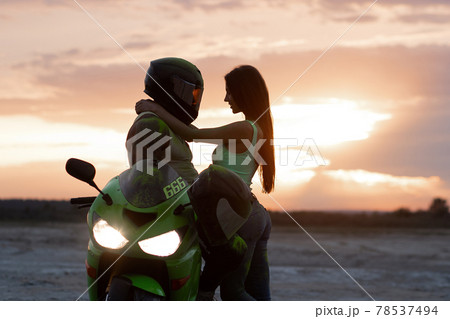 Couple embracing near motorbike on beach at sunset Couple embracing near motorbike on beach at sunset 78537494