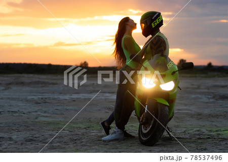 Couple embracing near motorbike on beach at sunset Couple embracing near motorbike on beach at sunset 78537496