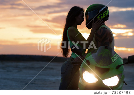 Couple embracing near motorbike on beach at sunset Couple embracing near motorbike on beach at sunset 78537498