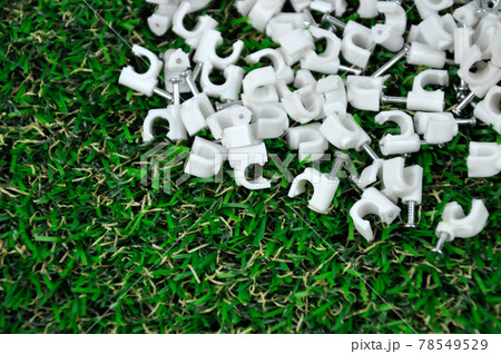 Plastic cable clip with concrete nail on the artificial grass.  78549529