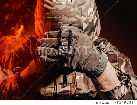 Soldier in uniform and helmet holding a cross necklace. 78549603