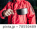 Hiker in red jacket holding metal cup. 78550489