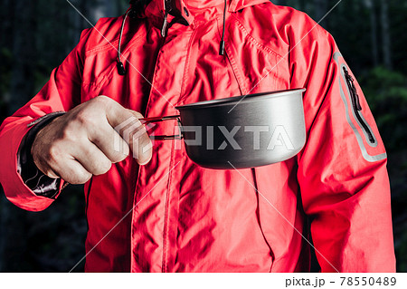 Hiker in red jacket holding metal cup. 78550489