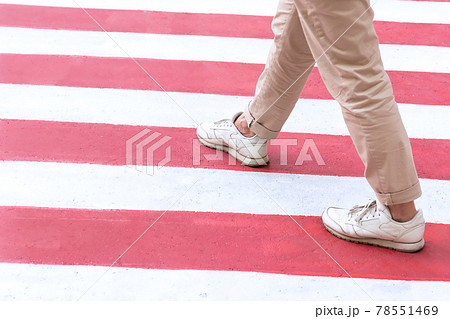 A woman in sportswear crosses a pedestrian crossing in red and white colors in the city. A woman in sportswear crosses a pedestrian crossing in red and white colors in the city. 78551469