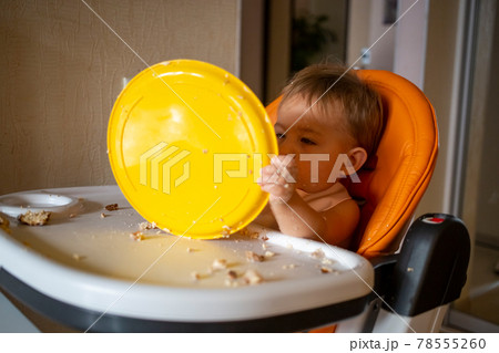 adorable baby plays with a plastic plate at the table. little child indulges in a baby chair after eating 78555260