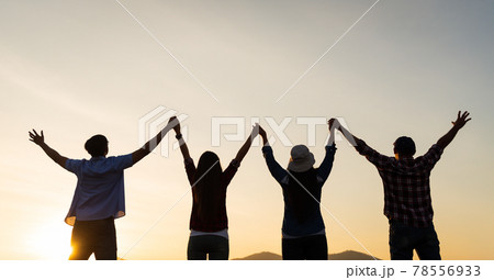 Group of happy friends are having fun with raised arms together in front of mountain and enjoy sunrise sunset showing unity and teamwork. Friendship happiness leisure partnership team concept. 78556933