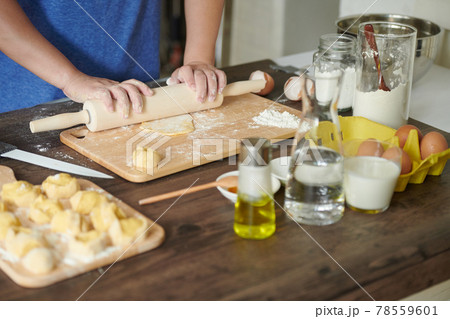 Female hands roll out a piece of dough with a rolling pin for making ravioli or dumplings on a wooden table sprinkled with flour. A step-by-step recipe for cooking ravioli or dumplings	 78559601