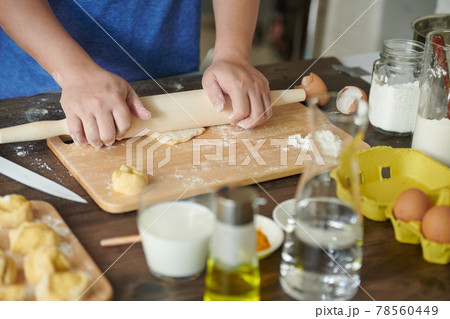 Female hands roll out a piece of dough with a rolling pin for making ravioli or dumplings on a wooden table sprinkled with flour. A step-by-step recipe for cooking ravioli or dumplings Female hands roll out a piece of dough with a rolling pin for making ravioli or dumplings on a wooden table sprinkled with flour. A step-by-step recipe for cooking ravioli or dumplings 78560449