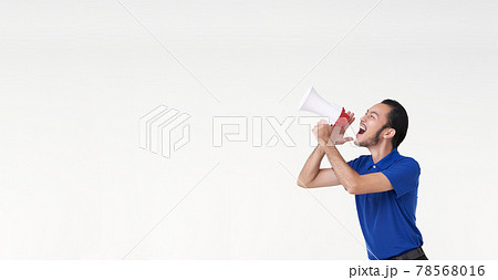 Happy young Asian man in blue shirt shouting announce into megaphone isolated on white background in studio. 78568016