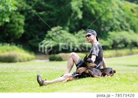 芝生で寛ぐ男性とドーベルマン 芝生で寛ぐ男性とドーベルマン 78573420