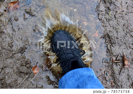 Water splash from shoes. Men's feet in hiking shoes steps into a puddle. Water splash from shoes. Men's feet in hiking shoes steps into a puddle. 78573738