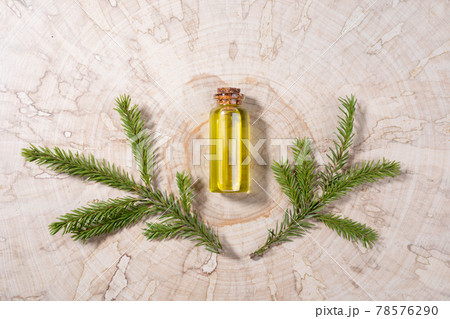 Small glass bottle with coniferous spa aromatic essential spruce oil and two small branches on wooden saw cut. Minimal Christmas aromatherapy and spa concept. View from above. Small glass bottle with coniferous spa aromatic essential spruce oil and two small branches on wooden saw cut. Minimal Christmas aromatherapy and spa concept. View from above. 78576290