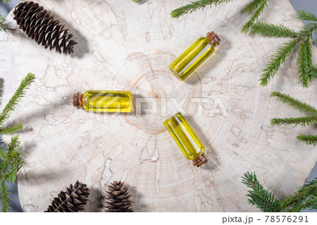 Christmas aromatherapy and spa creative concept with small glass bottles of coniferous spa aromatic essential spruce oil and green twigs and cones on wooden saw cut. View from above. Christmas aromatherapy and spa creative concept with small glass bottles of coniferous spa aromatic essential spruce oil and green twigs and cones on wooden saw cut. View from above. 78576291