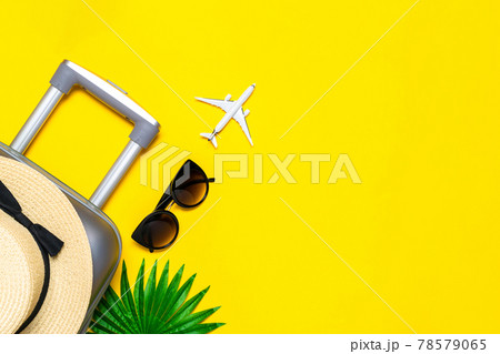 Summer background beach. Suitcase, sunglasses with palm leaves and straw hat, white plane in travel composition on yellow background. Tranquil beach scene with copy space. Summer background beach. Suitcase, sunglasses with palm leaves and straw hat, white plane in travel composition on yellow background. Tranquil beach scene with copy space. 78579065