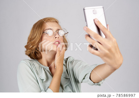 women with a mobile phone in their hands take pictures of themselves in a shirt on a light background 78586997