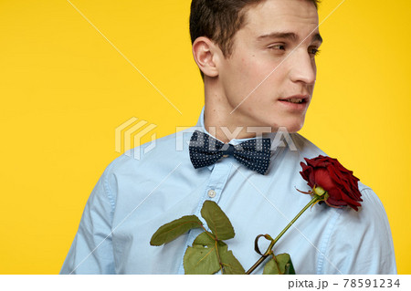 Elegant man in a suit with a red rose in his hands on a yellow background, cropped view Elegant man in a suit with a red rose in his hands on a yellow background, cropped view 78591234