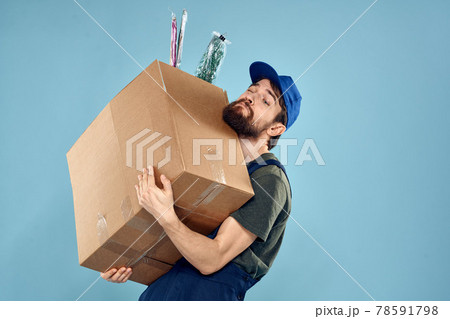 A man in working uniform with boxes in the hands of a carriage delivery service blue background A man in working uniform with boxes in the hands of a carriage delivery service blue background 78591798