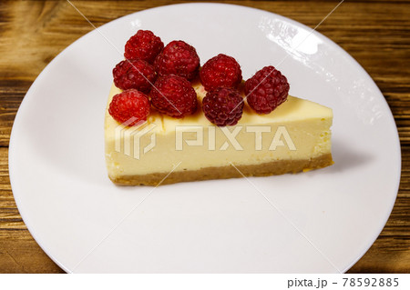 Piece of tasty New York cheesecake with raspberries in a white plate on wooden table Piece of tasty New York cheesecake with raspberries in a white plate on wooden table 78592885