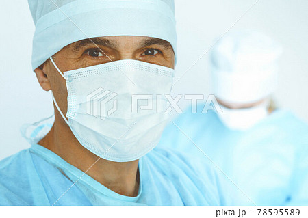 A male surgeon headshot, a group of surgeons is operating in the background. Health care concept 78595589