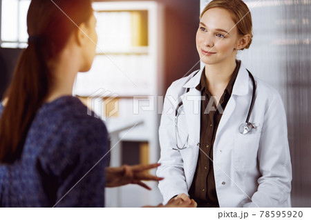 Cheerful smiling female doctor and patient woman discussing current health examination while sitting in clinic. Medical service in hospital. Medicine concept 78595920