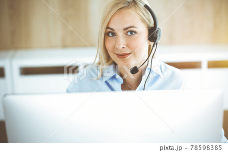 Blonde business woman sitting and communicated by headset in call center in sunny office. Concept of telesales business Blonde business woman sitting and communicated by headset in call center in sunny office. Concept of telesales business 78598385