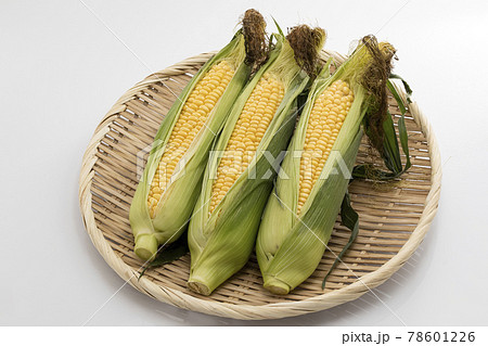 白バックでざるに乗せたひげ付きのとうもろこしの写真素材