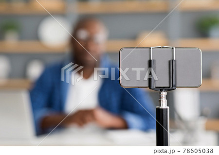 Mature black man blogger broadcasting from home, talking to phone camera, selective focus on smartphone 78605038