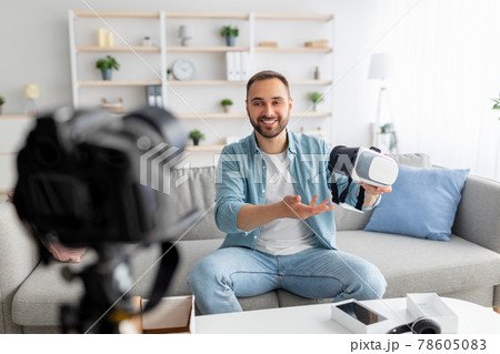 Young male blogger shooting video review of virtual reality headset, using professional camera at home 78605083