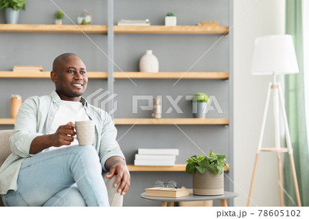 Smiling and thoughtful african american man drinking coffee, sitting in armchair in living room interior, free space Smiling and thoughtful african american man drinking coffee, sitting in armchair in living room interior, free space 78605102