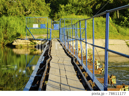 A pedestrian steel bridge with railings and a wooden floor runs through the river dam. 78611177