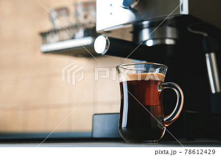 Transparent cup coffee close-up front view. Home coffee maker and process of making coffee drink. Defocus from coffee beans and copy space. 78612429