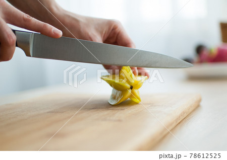 Female hands are holding knife and cutting exotic ripe starfruit or averrhoa carambola. Healthy food, fresh organic star apple fruit. 78612525