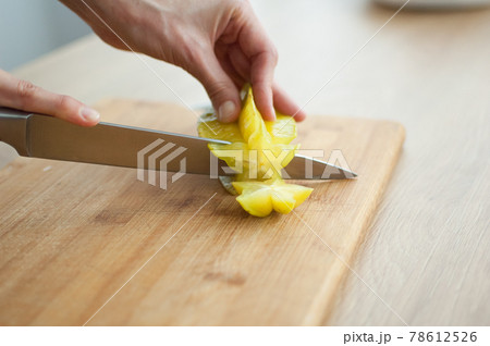 Female hands are holding knife and cutting exotic ripe starfruit or averrhoa carambola. Healthy food, fresh organic star apple fruit. 78612526