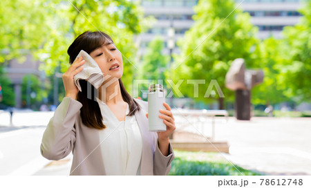 外で汗を拭きながら水分補給をするビジネスウーマン 外で汗を拭きながら水分補給をするビジネスウーマン 78612748