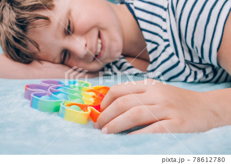 Smiling boy playing with rainbow pop it fidget toy. Push bubble fidget sensory toy - washable and reusable stress relief toy. Antistress toy for child with special needs. Mental health concept Smiling boy playing with rainbow pop it fidget toy. Push bubble fidget sensory toy - washable and reusable stress relief toy. Antistress toy for child with special needs. Mental health concept 78612780