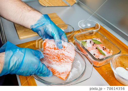 The cook in hygienic gloves prepares lightly salted salmon.  78614356