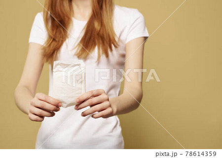 Girl with pad on beige background menstruation critical days cropped view of white t-shirt 78614359