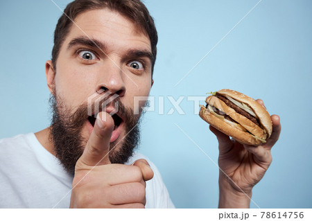 Emotional man hamburger fast food diet food close-up blue background Emotional man hamburger fast food diet food close-up blue background 78614756